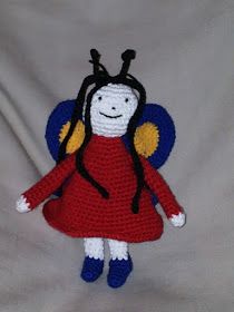 a crocheted doll with a red dress and yellow wings on it's head