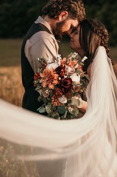 a bride and groom are standing in a field with their veil blowing in the wind