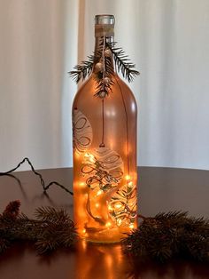 a bottle with lights in it sitting on a table next to evergreen branches and pine cones