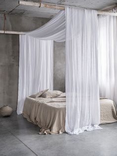 a bed with white drapes hanging from it's sides and pillows on the floor