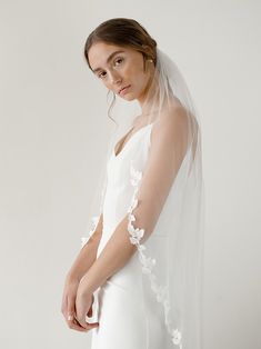 a woman wearing a wedding veil with white flowers on the side and long sleeves over her shoulder