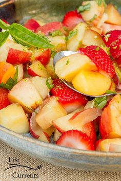 a close up of a bowl of fruit with a spoon in it and strawberries on the side