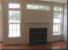 an empty living room with two windows and a fireplace