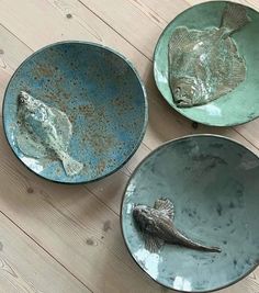 three plates with fish on them sitting on a wooden floor