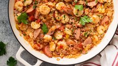 a skillet filled with shrimp and rice on top of a striped towel next to parsley