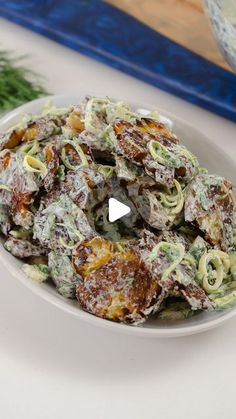 a white plate topped with pasta salad next to a bowl filled with sauce and parsley