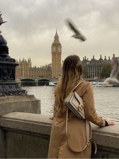 a woman is looking at the birds flying over the water in front of big ben