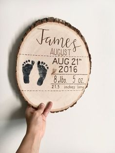 a hand holding up a wooden sign with baby's footprints on it and the date