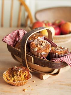 some muffins are sitting in a basket on a table next to an apple bowl