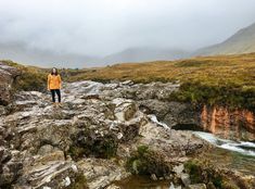 a man standing on top of a rocky cliff next to a river