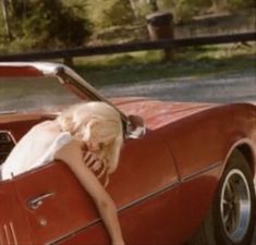 a woman leaning on the back of a red car with her head in the trunk