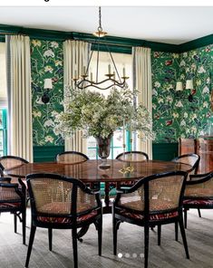 a dining room with green wallpaper and wooden table surrounded by chairs in front of windows