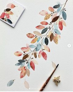 a watercolor painting of leaves on a white paper next to a paintbrush and pencil