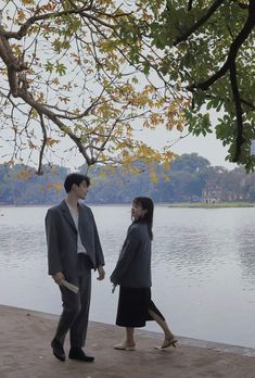 two people standing next to each other near the water