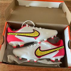 a pair of white and pink nike soccer cleats in a box on a wooden floor