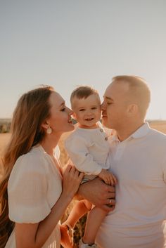 a man and woman holding a baby while standing in the middle of an open field