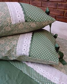 two green and white pillows sitting on top of a bed next to a brick wall