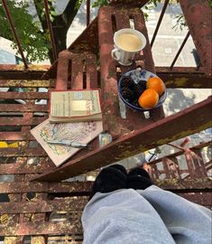 someone's feet resting on a bench with books and oranges