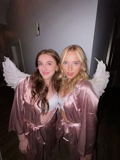 two beautiful young women dressed in pink and white robes posing for the camera with angel wings on their shoulders