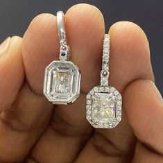 a pair of diamond pendants are shown in the foreground, with one being held up by someone's hand