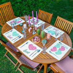 a wooden table with place mats and napkins on it in the middle of a grassy area