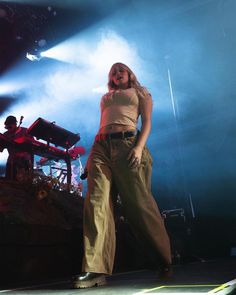 a woman standing on top of a stage with her hands in her pockets and wearing wide legged pants