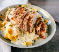 a white plate topped with pasta and sliced chicken breast on top of cheese covered noodles