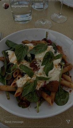 a white plate topped with pasta covered in cheese and spinach leafy toppings