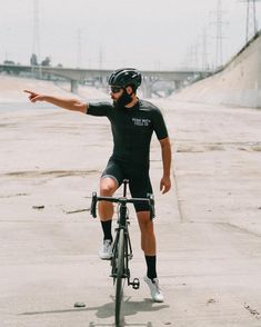 a man riding a bike on top of a cement ground next to a bridge and holding his arm out