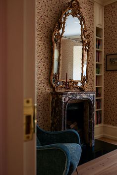 a room with a chair, fireplace and mirror on the wall next to it's bookshelf