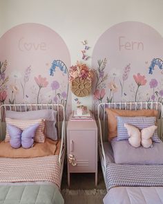 two twin beds with pink and purple comforters in a girls'room, the wall has flowers painted on it