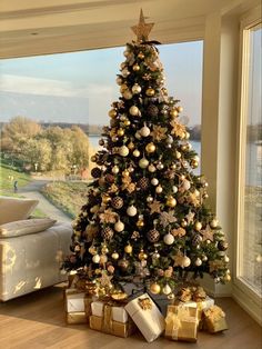 a decorated christmas tree with gold and silver ornaments in front of a large window overlooking the water