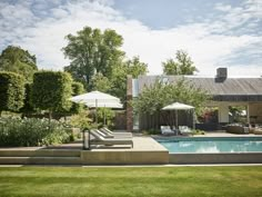 an outdoor swimming pool with lounge chairs and umbrellas in front of the house on a sunny day