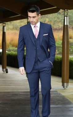 a man in a blue suit and pink tie walks down a walkway with his hands in his pockets