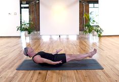 a man laying on top of a yoga mat in a room next to a plant