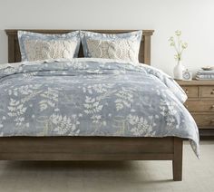 a bed with blue and white comforter on top of it in a bedroom next to a dresser