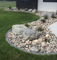 a rock garden in front of a house with grass and rocks on the ground next to it