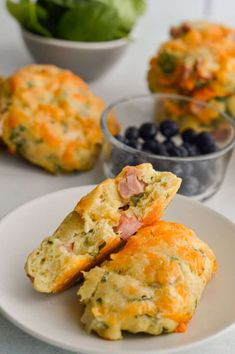 two muffins on a plate with blueberries and spinach in the background