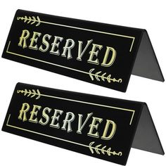 two black and gold reserved signs with arrows on each side, one has the word reserved printed on it