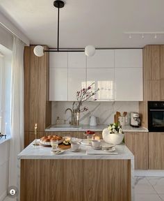 a white kitchen with wooden cabinets and marble counter tops is pictured in this image, there are candles on the island