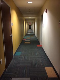 a long hallway with carpeted floors and lights on either side of the corridor, leading to another room