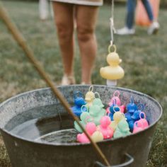 a bucket full of rubber ducks in the grass next to a person holding a broom