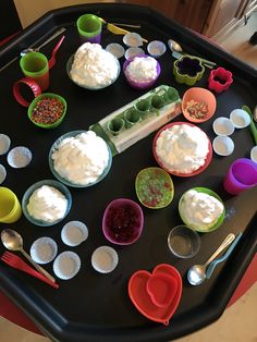 an assortment of desserts are arranged on a black tray with spoons and cups