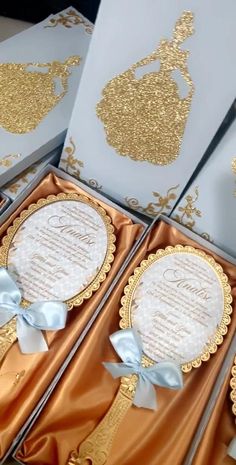 two wedding cards in gold and white with bows on them, sitting next to each other