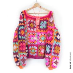 a colorful crocheted sweater hanging on a wooden hanger with a tag attached to it