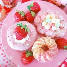 three donuts and two strawberries on a pink plate with polka dot table cloth