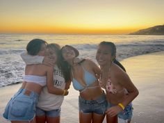 three girls standing on the beach at sunset with their arms around each other's shoulders