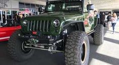 a green jeep parked in front of a red truck at a showroom with people walking around