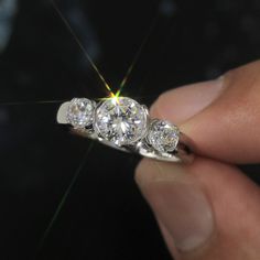 three stone diamond ring being held up by someone's hand with the light shining through it