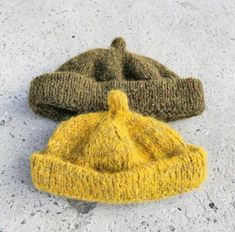 two knitted hats laying on the ground next to each other, one yellow and one green